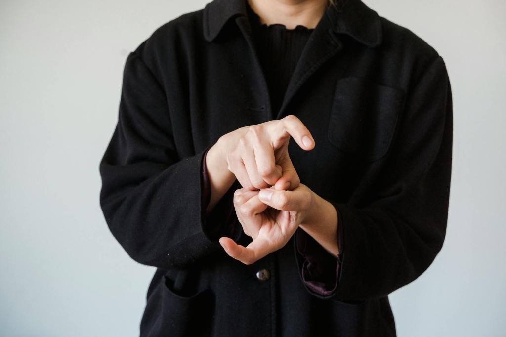 A person in a black front-button shirt signs something that might be the start of the "change" sign with two "X" handshapes.
