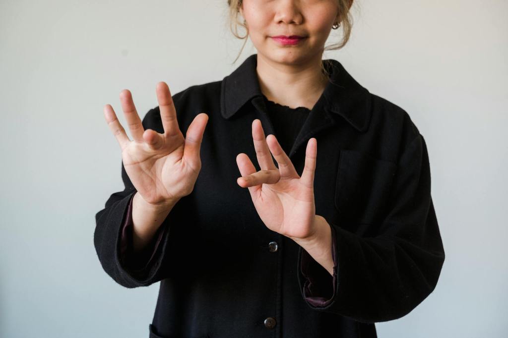 An asian woman in a black front-button shirt signs "sympathy" with two hands, using the "25" handshapes.